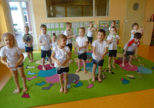 Dzieci przesuwają stopami butelki plastikowe po dywanie.